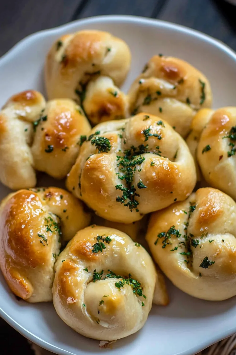 Ein Teller mit knusprig gebackenen Knoblauchknoten, glasiert mit Kräuterbutter und bestreut mit frischer Petersilie.