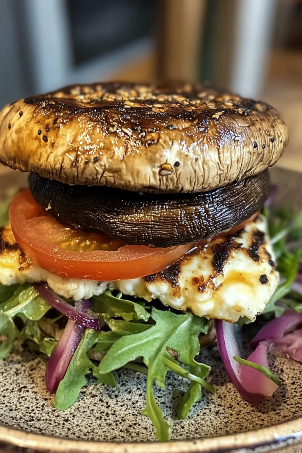 Grilled portobello mushroom burger with grilled halloumi cheese, fresh tomato, arugula, and red onions on a plate.