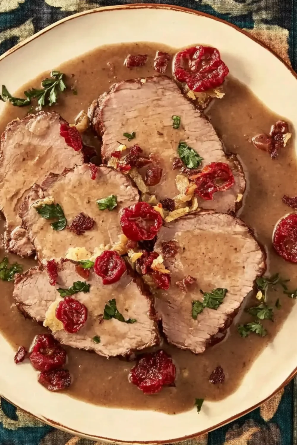 Zartes Sauerbraten, in Scheiben geschnitten, serviert mit einer würzigen Bratensoße, getrockneten Tomaten und frischer Petersilie.