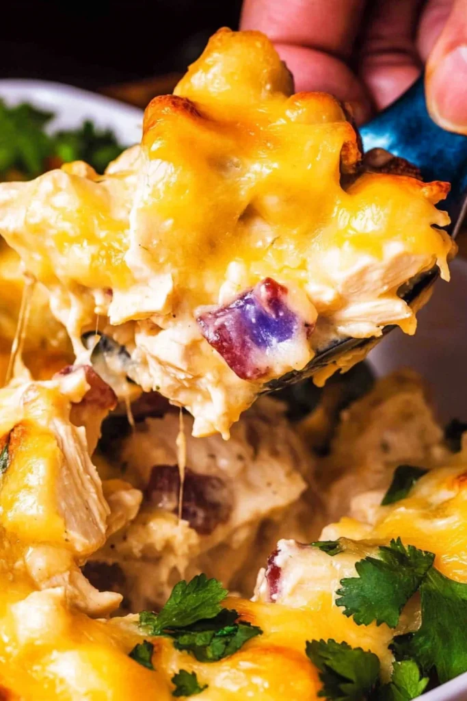 Ein Stück Keto-Hähnchen-Bacon-Ranch-Auflauf wird mit einem Löffel aus der Auflaufform genommen. Die cremige, käsige Oberfläche zieht Fäden, während das Stück Stücke von Hähnchen und Speck enthält.