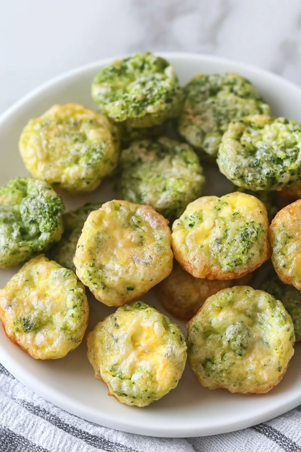 Eine Platte mit kleinen Brokkoli-Ei-Bissen, die goldbraun und lecker aussehen.