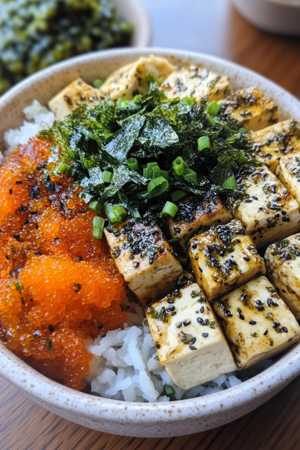 Eine Schale mit Reis, mariniertem Tofu, Seetang, Frühlingszwiebeln und Fischrogen in einer Schüssel, die ein köstliches und gesundes Poke-Bowl-Gericht bildet.