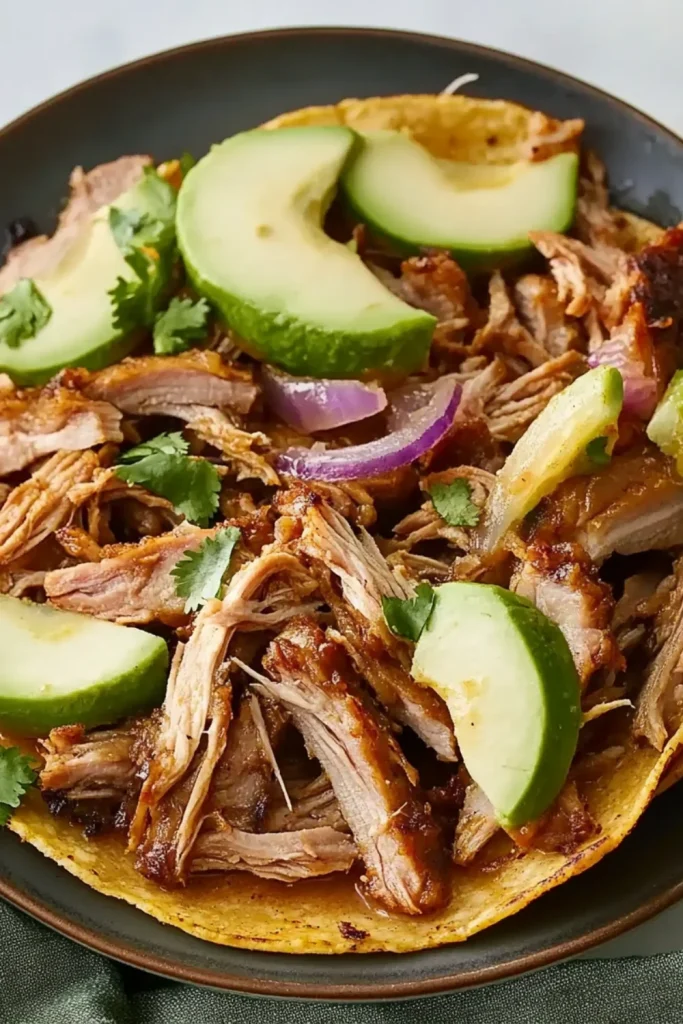 Pork Carnitas mit zartem, langsam gegartem Schweinefleisch, frischen Avocadoscheiben, Zwiebeln und Koriander auf einer weichen Tortilla.