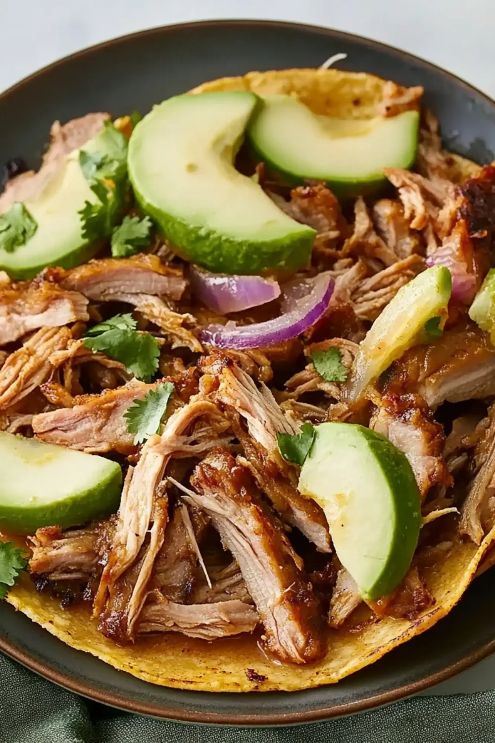Pork Carnitas mit zartem, langsam gegartem Schweinefleisch, frischen Avocadoscheiben, Zwiebeln und Koriander auf einer weichen Tortilla.