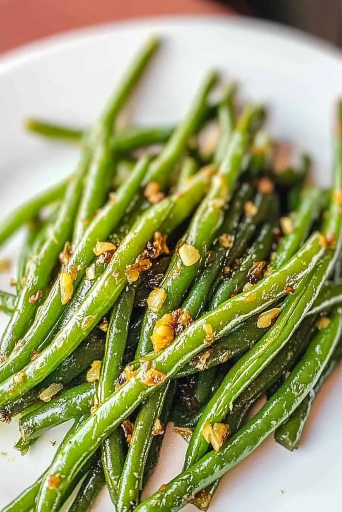 Glänzend gebratene grüne Bohnen mit gehacktem Knoblauch, serviert auf einem weißen Teller.