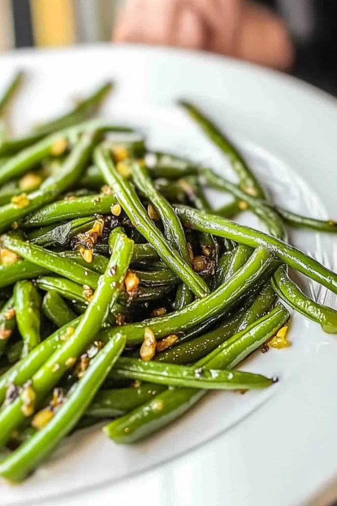 Glänzend gebratene grüne Bohnen mit gehacktem Knoblauch, serviert auf einem weißen Teller.